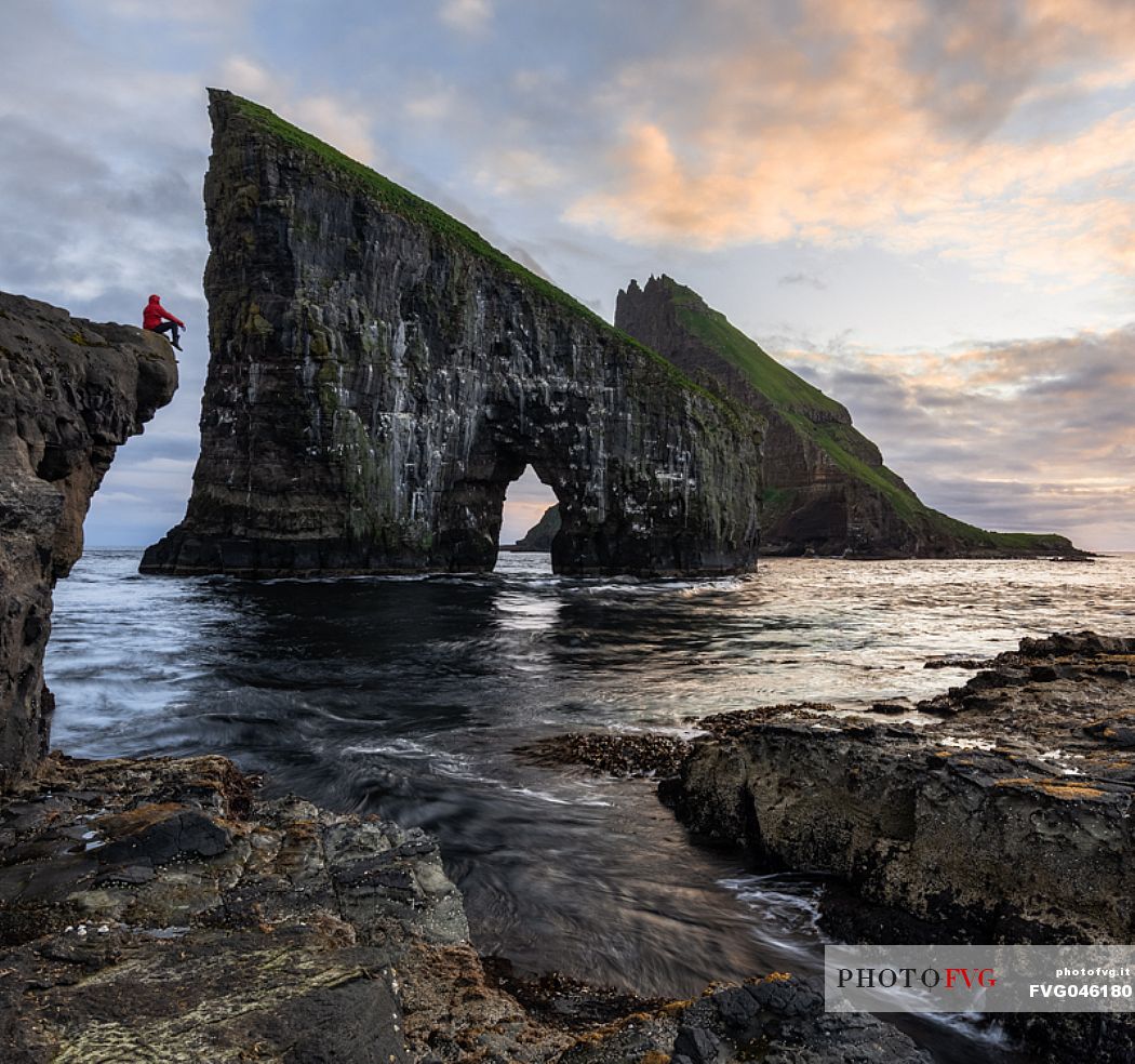 Tourist looking the Drangarnir rocks, a collective name of two sea stacks, which are called Stri Drangur (large rock) and Ltli Drangur (small rock) respectively, and are located next to each other between the islands of Vgar and Tindhlmur, Srvgsfjrur Fjord near Srvgur, Faeroe islands, Denmark